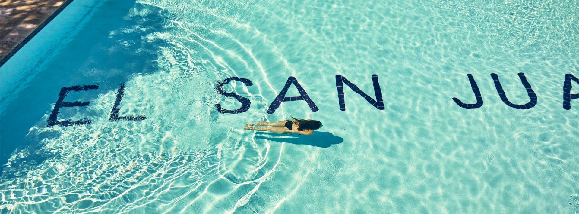 woman swimming in a pool that has el san juan written on the bottom