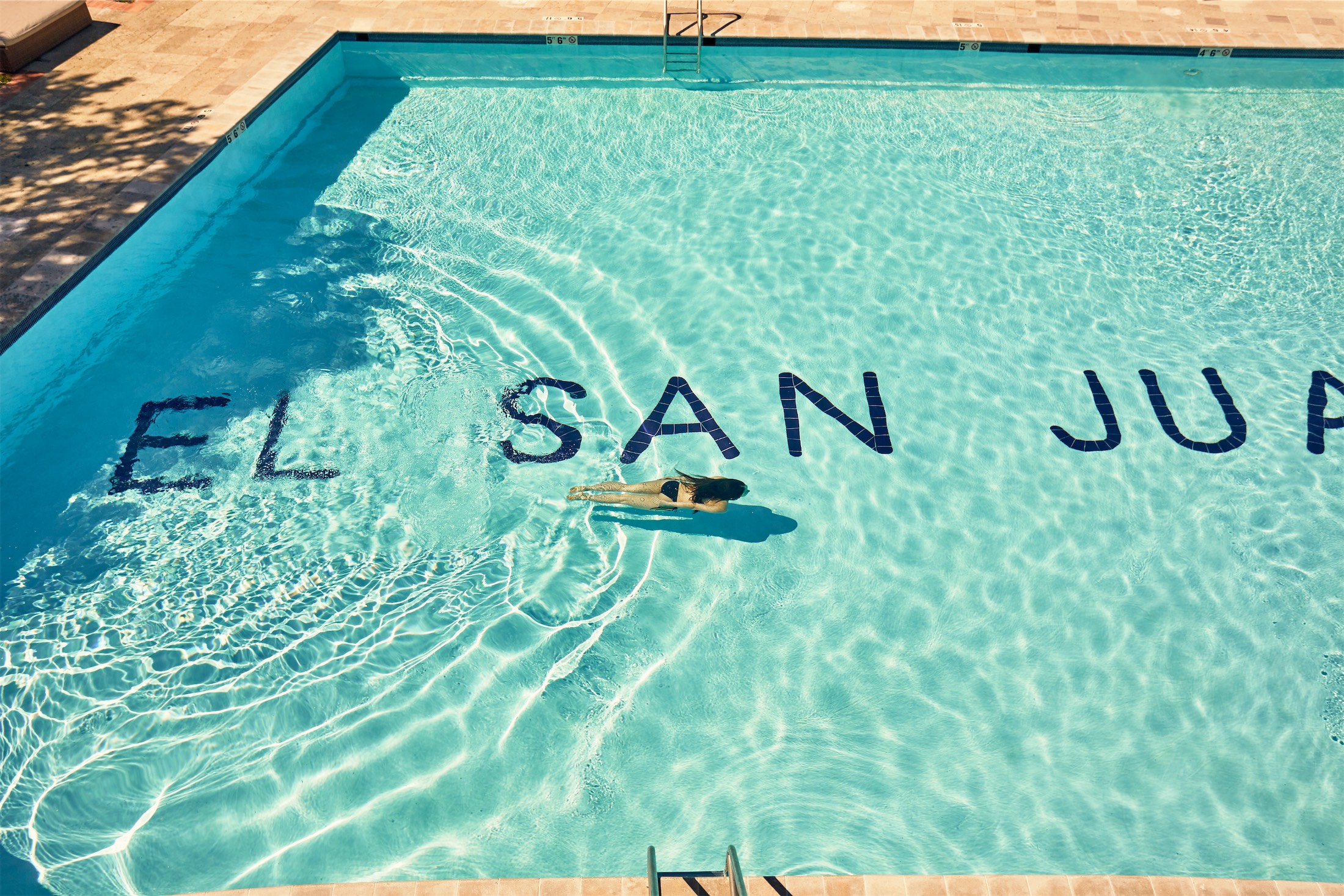 woman swimming in a pool that has el san juan written on the bottom