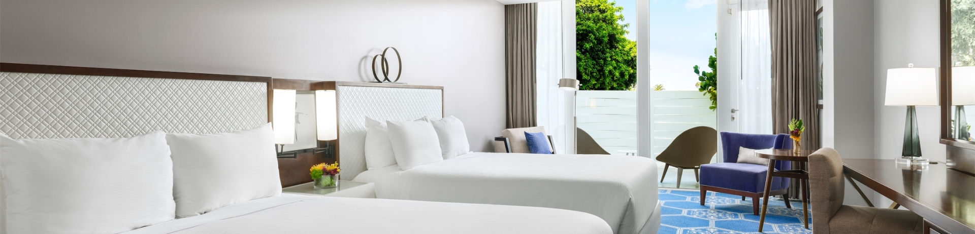 two queen sized beds in a room with a desk and cushioned seating