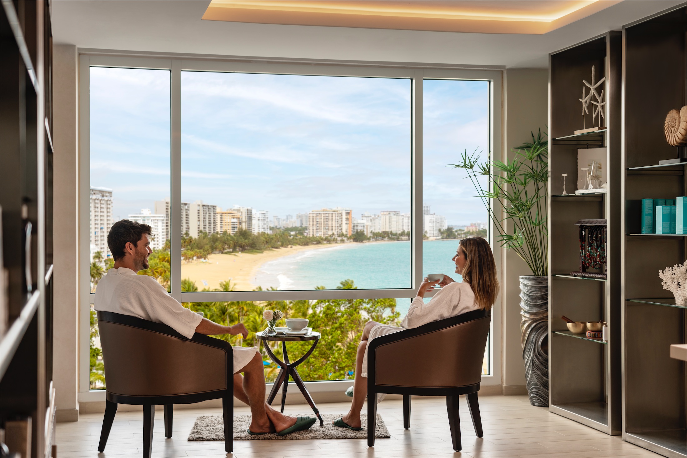 couple in bathrobes sitting by a window overlooking the beach