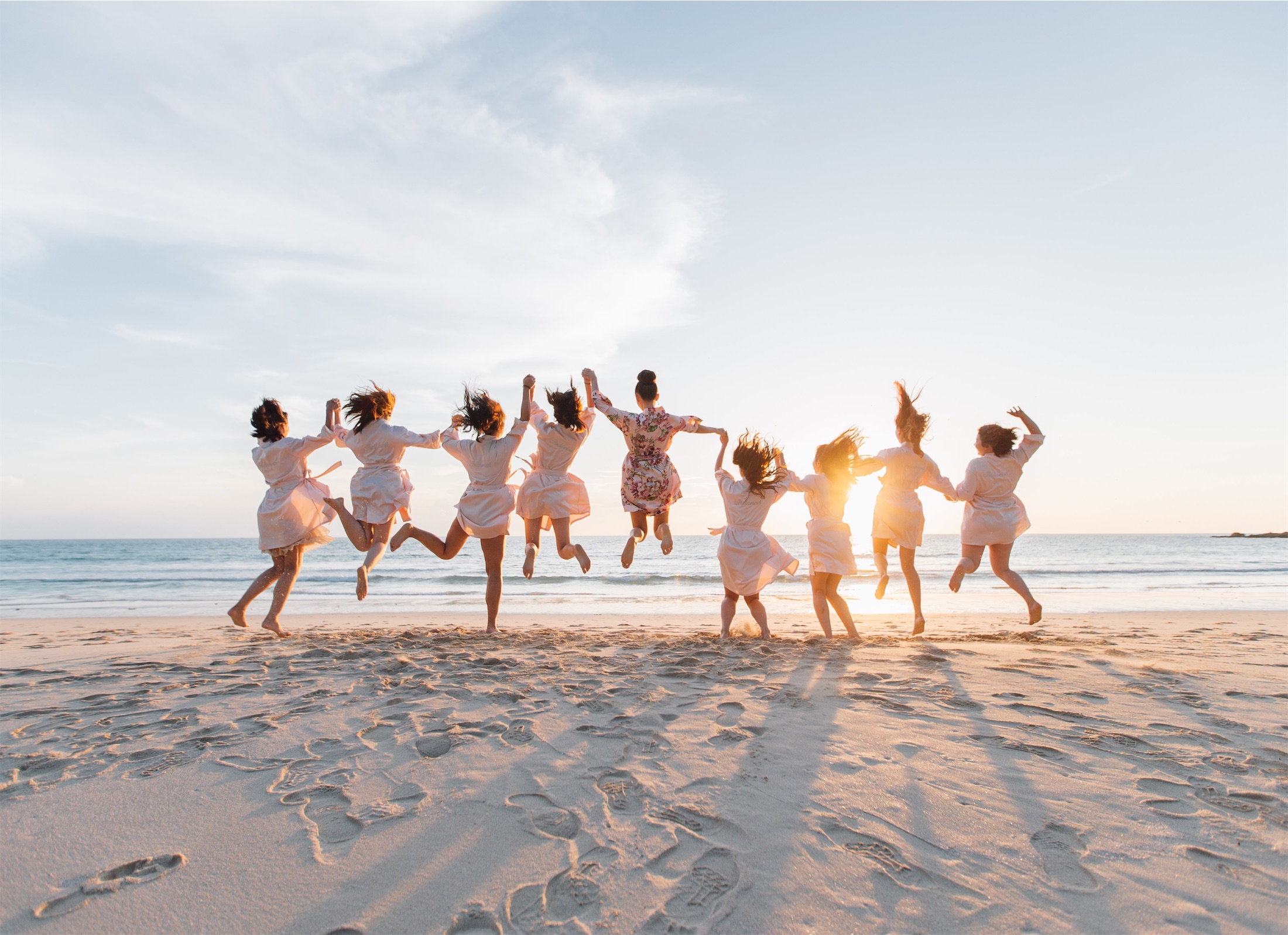 group of friends holding hands and jumping on the beach